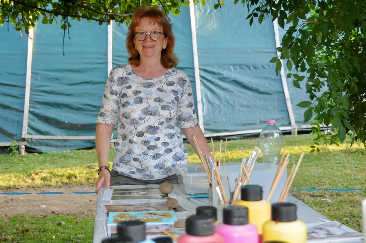 Man sieht eine Frau mit vielen Pinseln und Farbflaschen.
